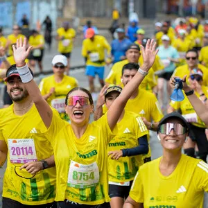 Mujer sonriendo con las manos arriba rodeada de más atletas corriendo