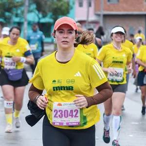 Mujer enfocada mirando al frente mientras corre con gorra naranja