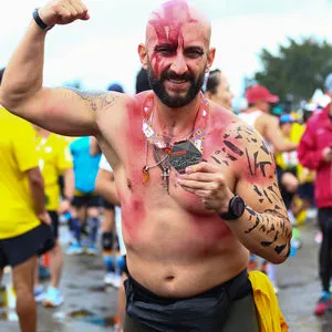 Hombre disfrazado enseña su medalla al terminar carrera