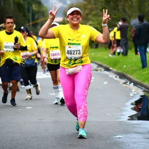 Mujer con pantalón rosa sonríe mientras levanta ambas manos